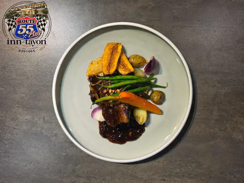 A plated braised beef dish with vegetables served at Route 55+