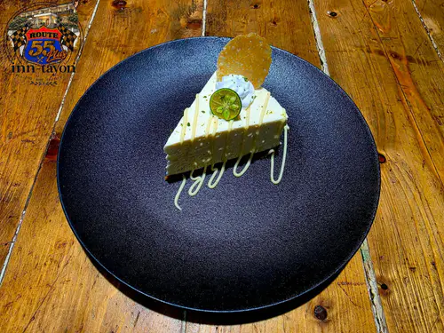 A slice of creamy citrus pie with a lime slice on a dark plate over a rustic wooden table