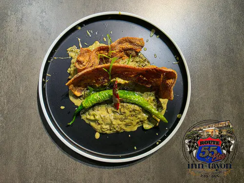 Crispy pork belly with grilled green chili on a creamy bed, served on a dark plate